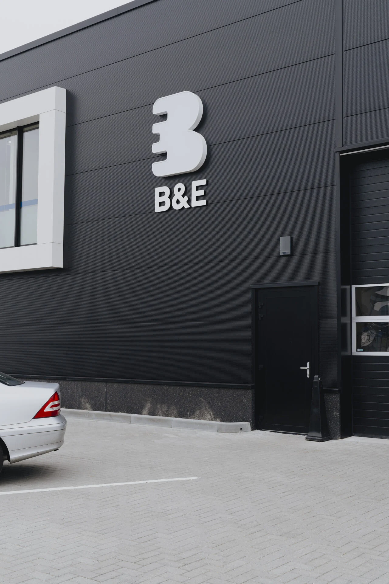 Gevelreclame met witte losse letters B&E op donkere bedrijfsgevel